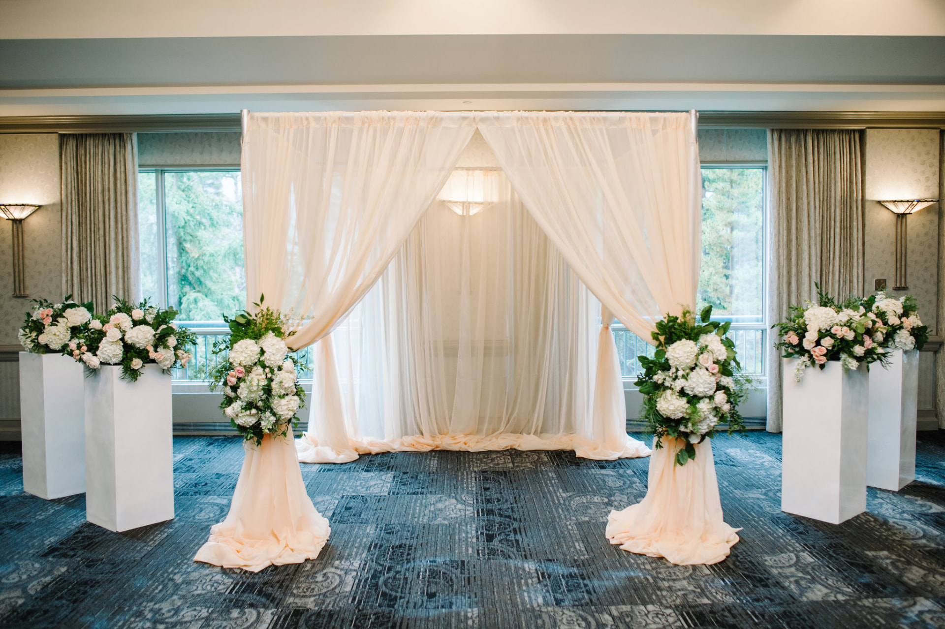 Indoor ceremony with a peach draped backdrop and white and pink floral pillars in Banff