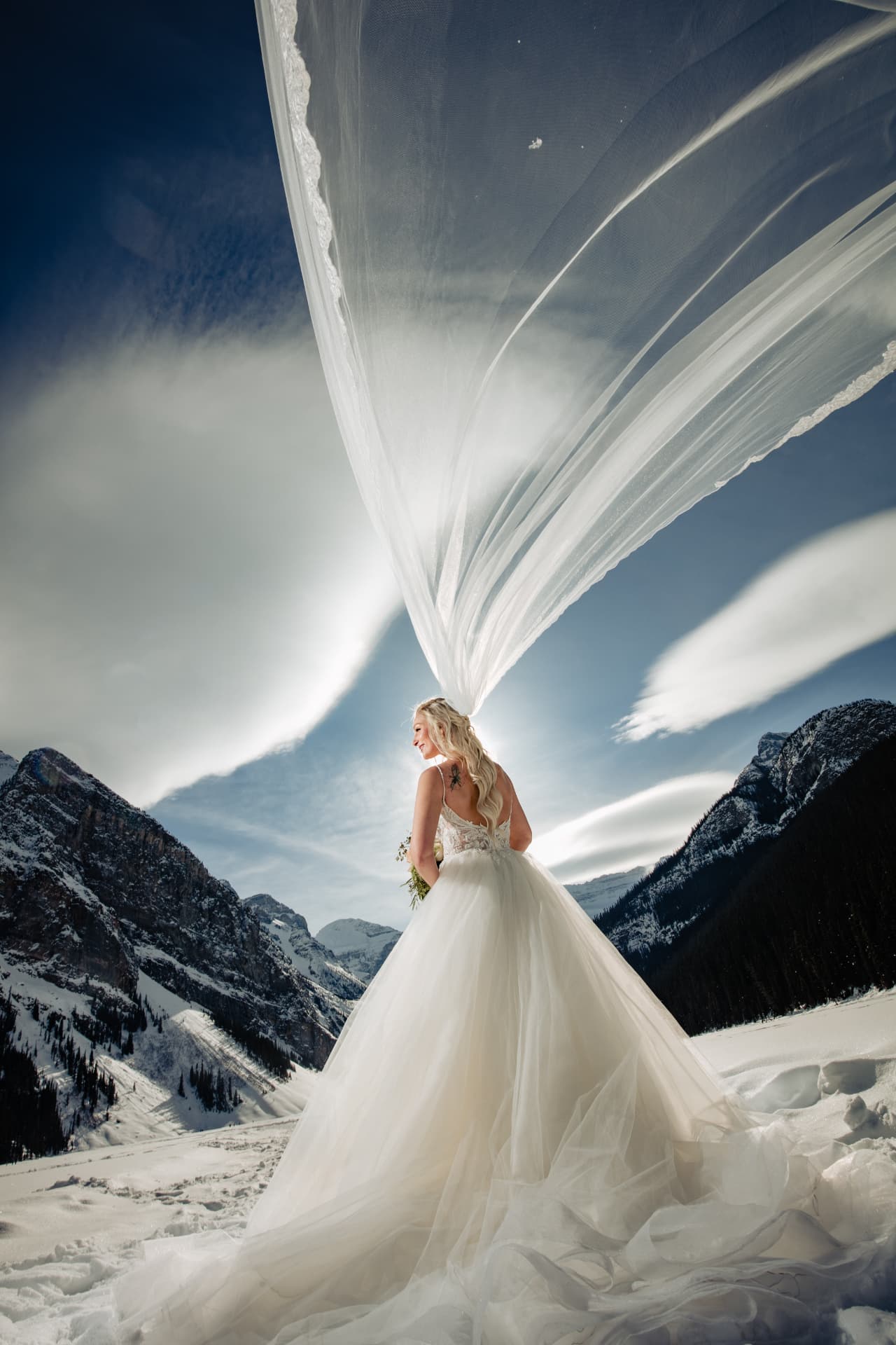 Bride's cathedral veil lifting in the wind against the snow-covered Rockies at Lake Louise