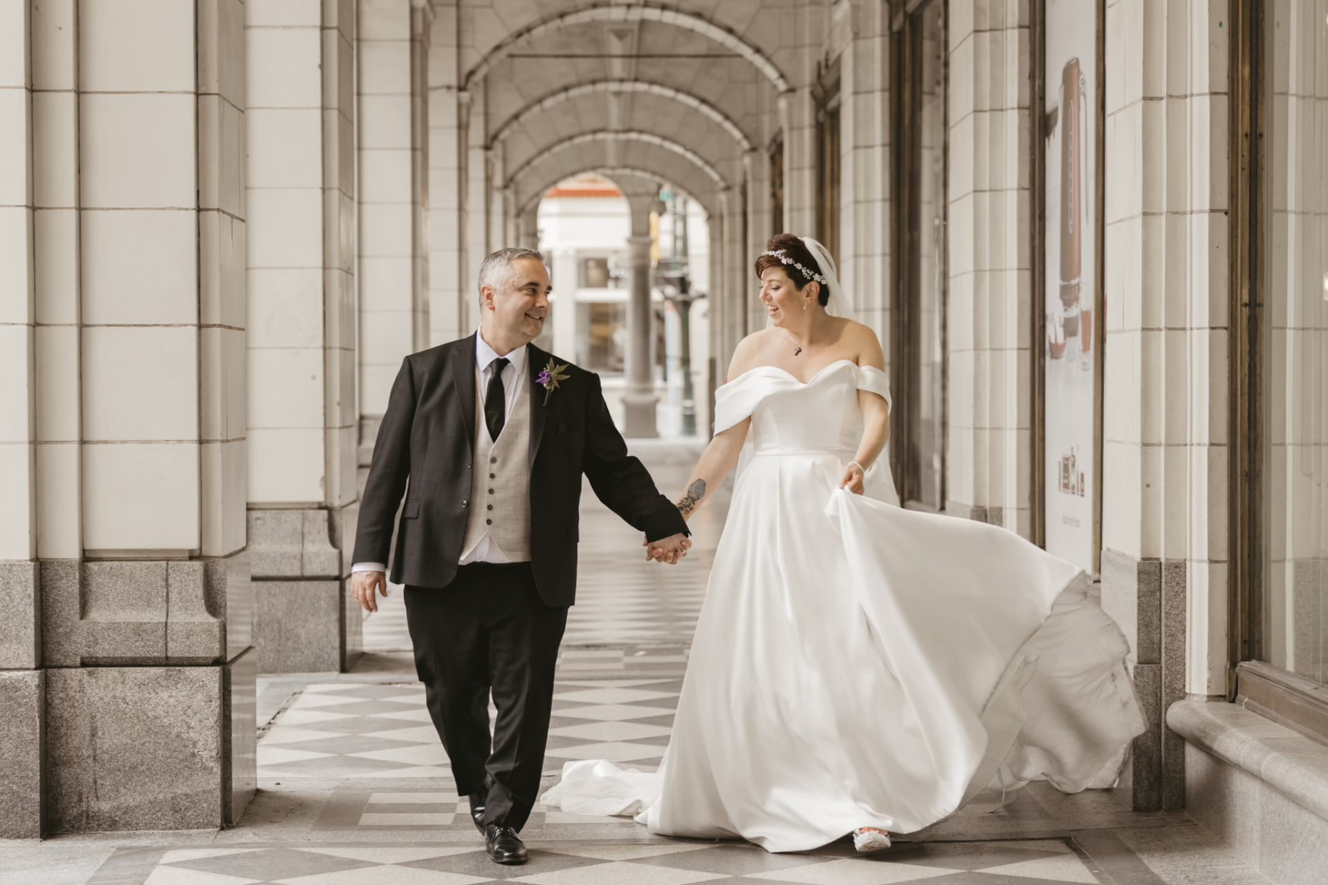 Bride and groom walking hand in hand through a white stone arcade in downtown Calgary