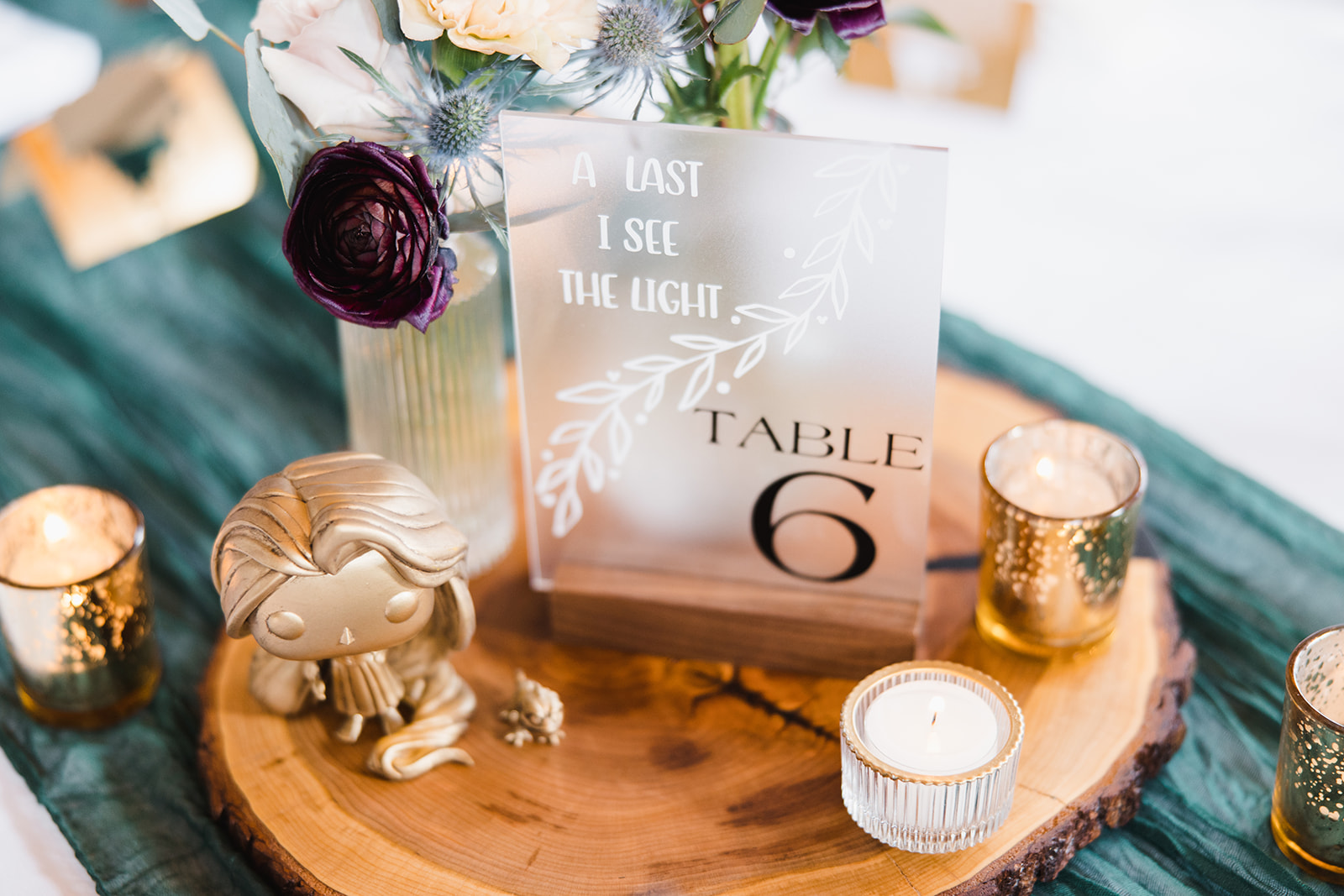 Frosted acrylic table number on a wood round with candlelight and burgundy ranunculus