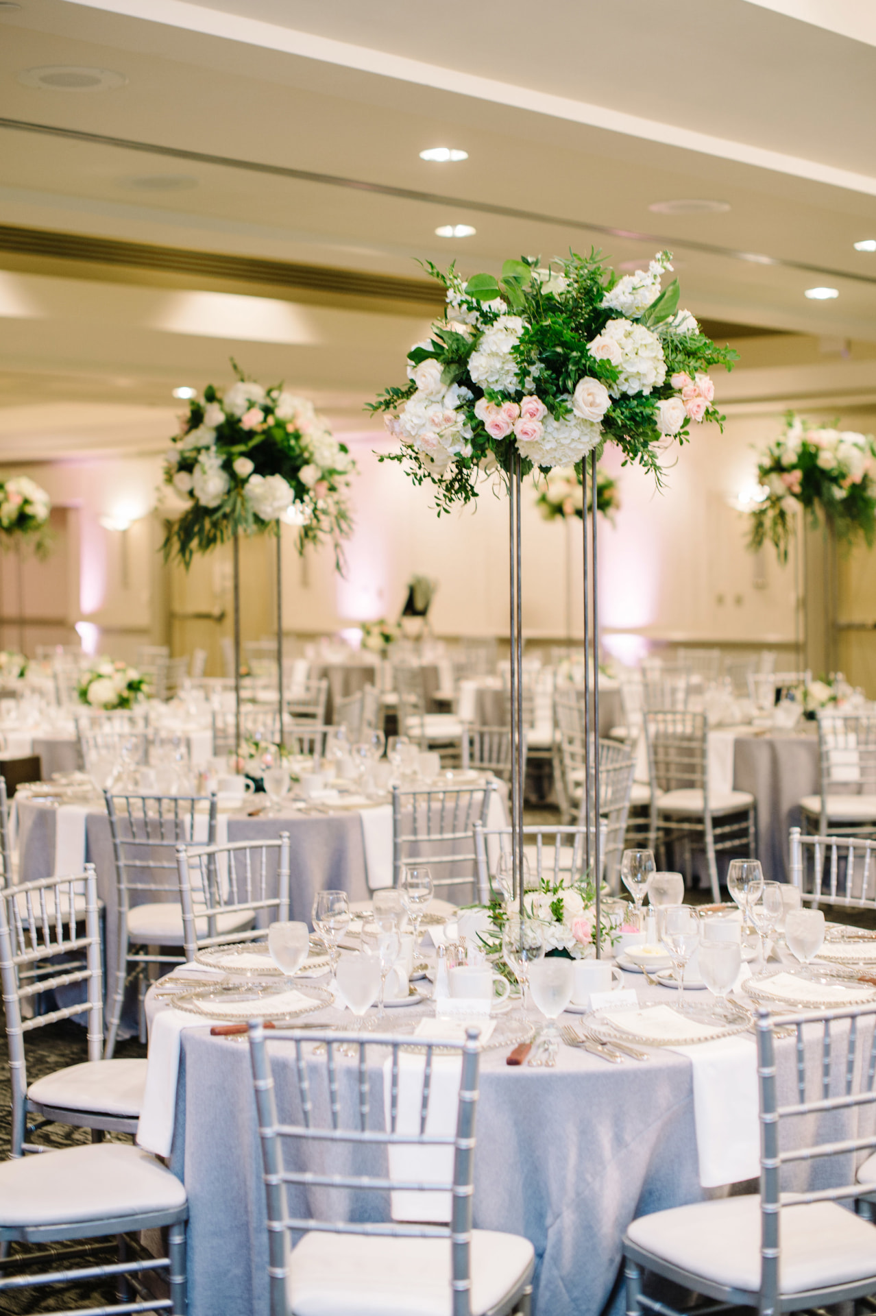 Reception ballroom with tall white and blush floral centrepieces and silver chairs