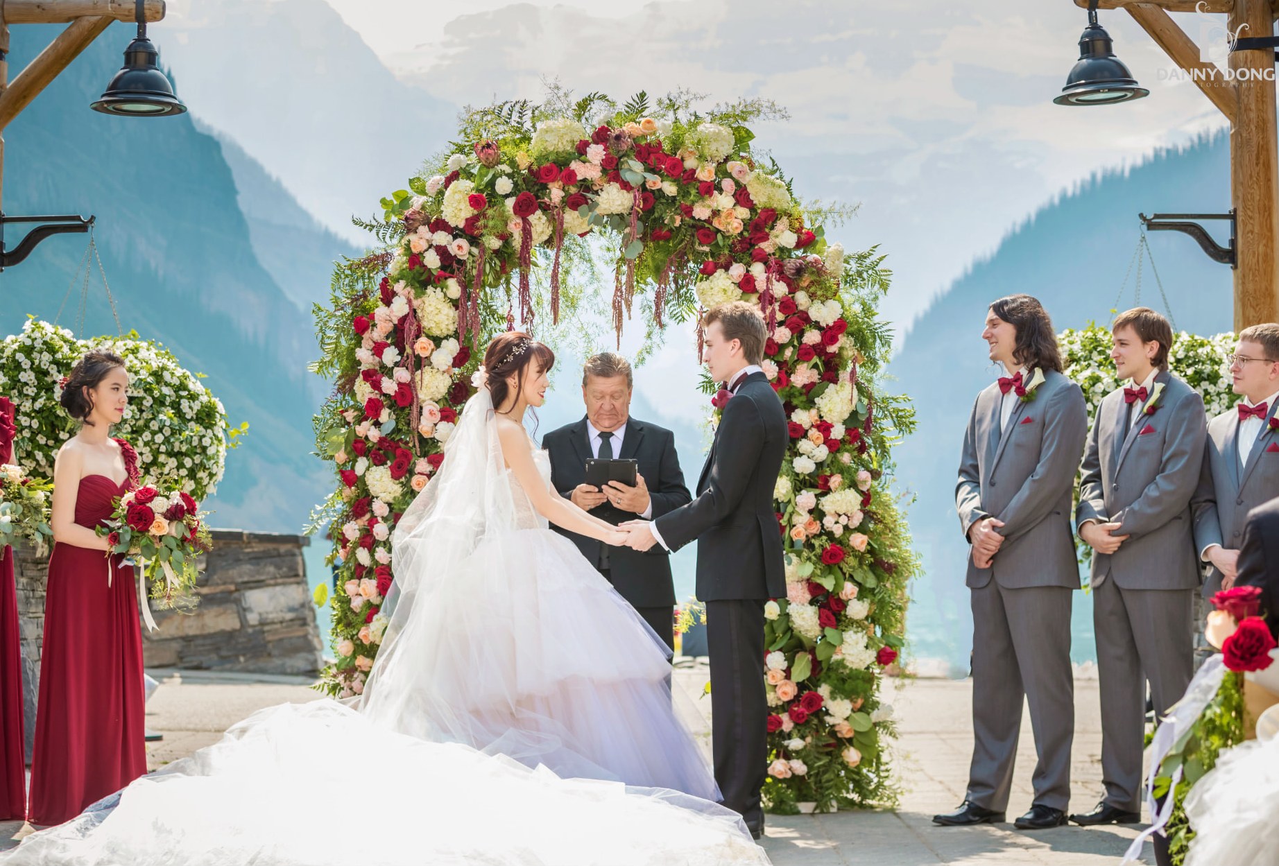 Ceremony beneath a red and blush floral arch overlooking Lake Louise