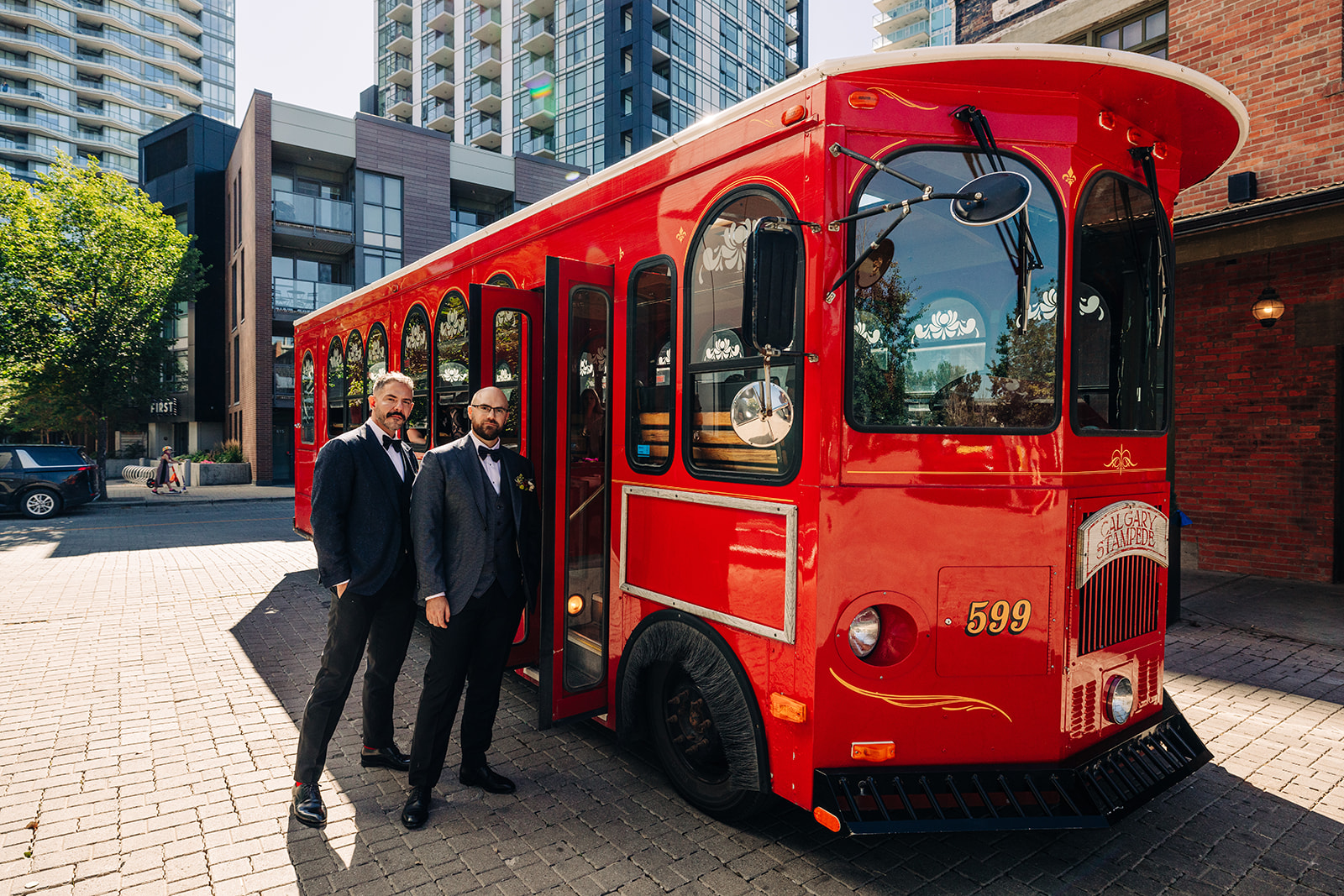 Two grooms in front of a vintage red Stampede trolley in downtown Calgary