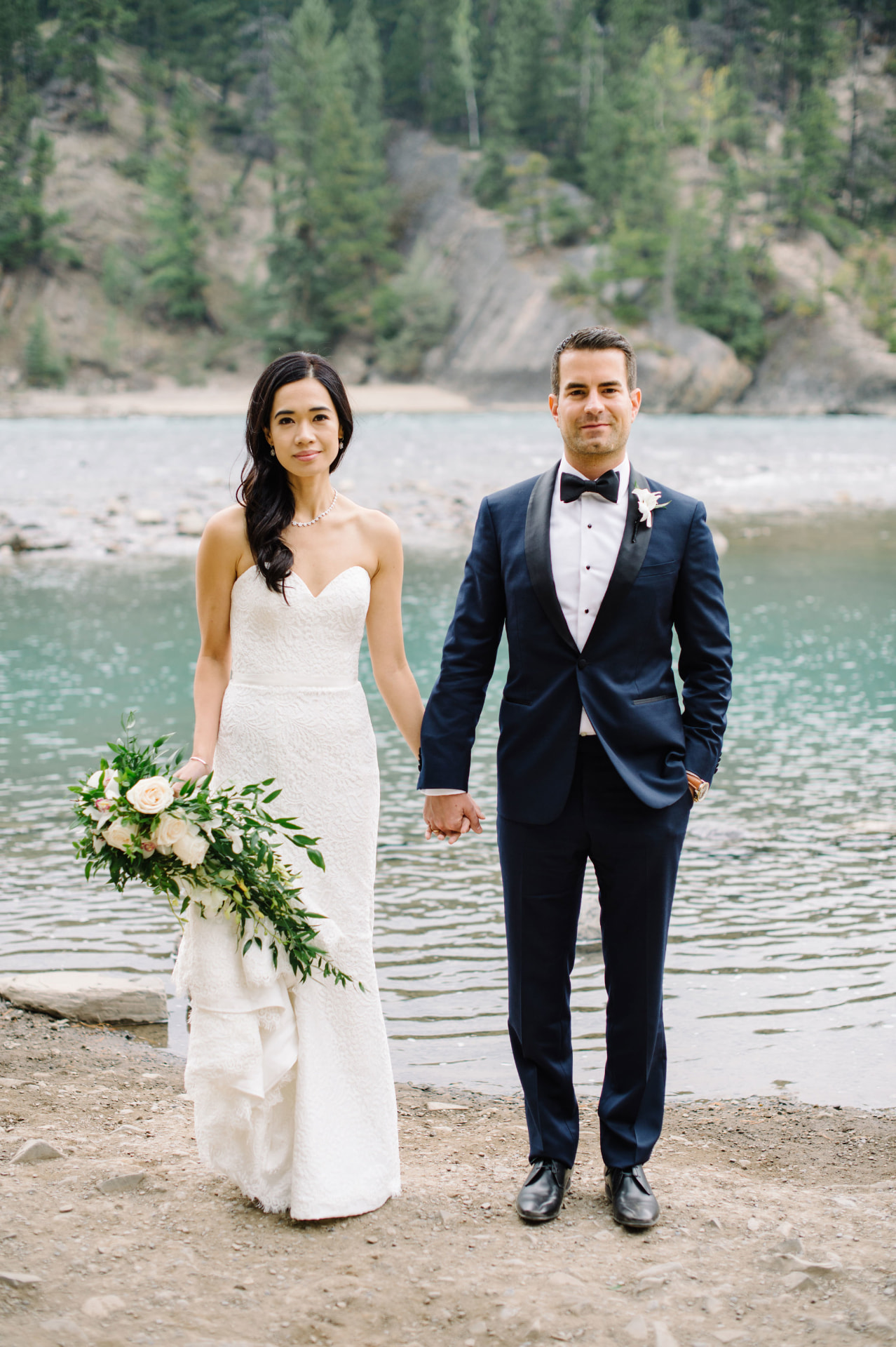 Couple holding hands beside a turquoise mountain river near Banff
