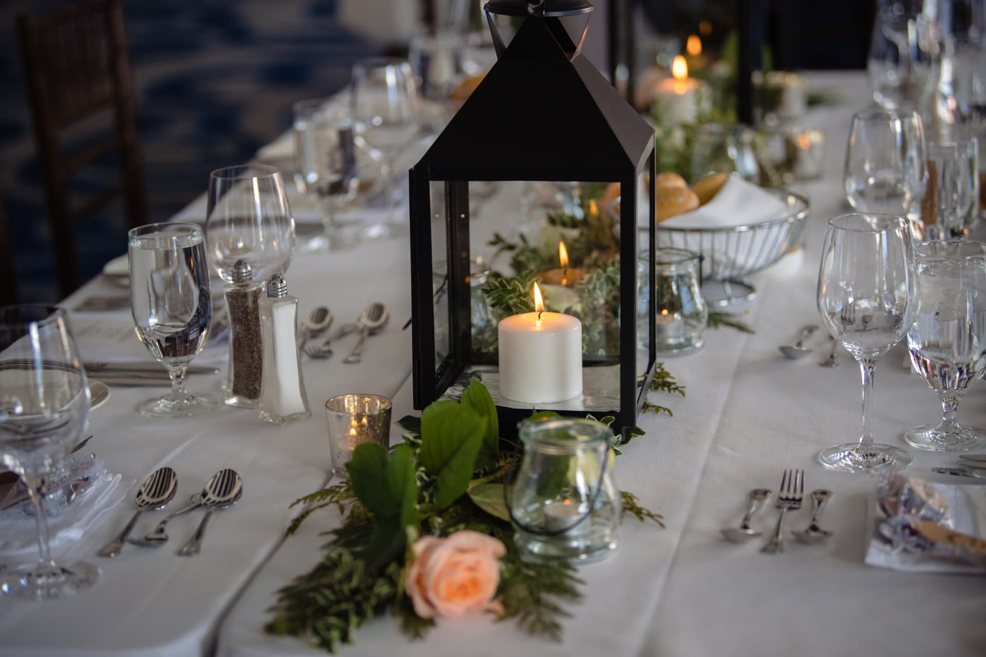 Long reception table with black lanterns, cedar garland and blush garden roses